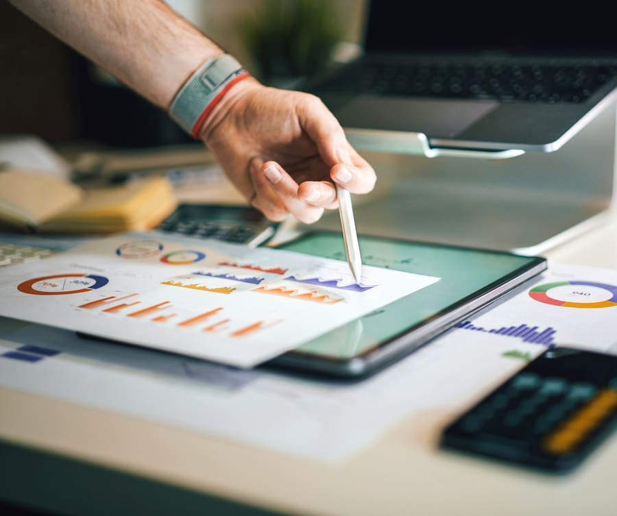 A stylus on a tablet, printed charts spread across the desk
