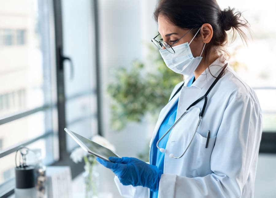 A pharmacist in a mask and gloves reviewing a claim on a tablet