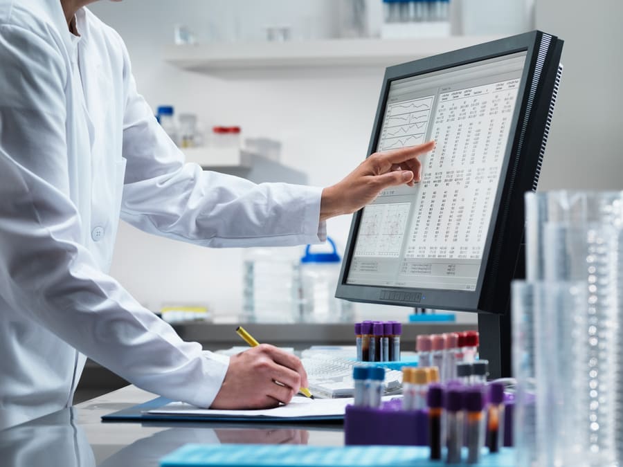 A pharmacist checking figures on screen beside racked sample tubes