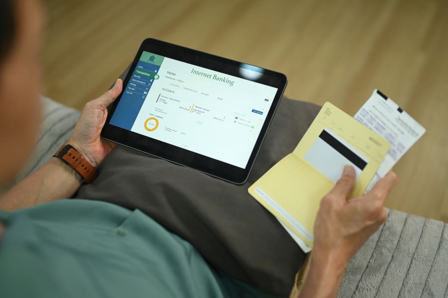 Hands holding a tablet over a desk, an account summary on screen