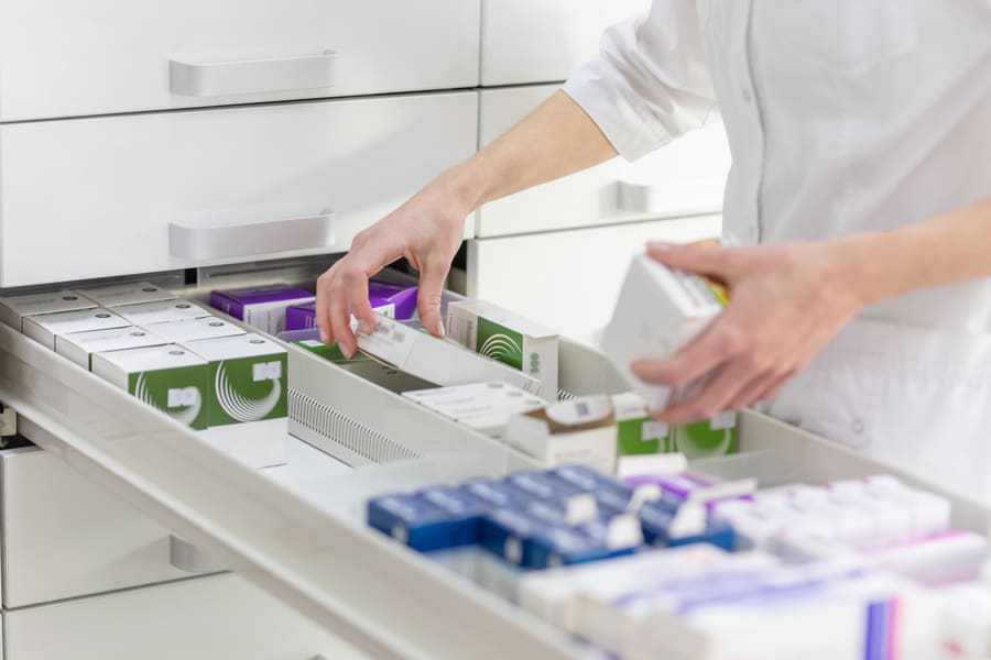 A pharmacy assistant picking medication cartons from a dispensary drawer