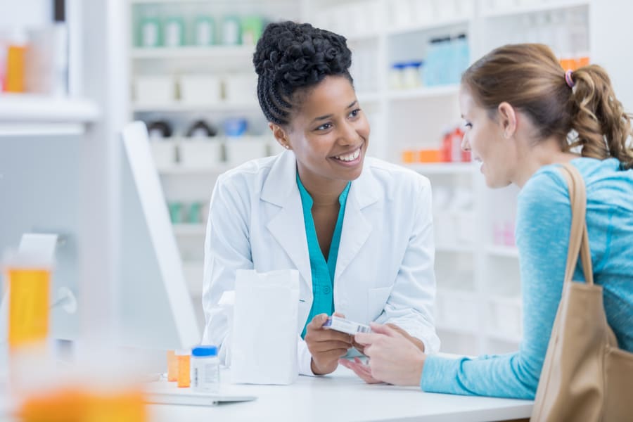 A pharmacist handing a packed order across the counter to a patient