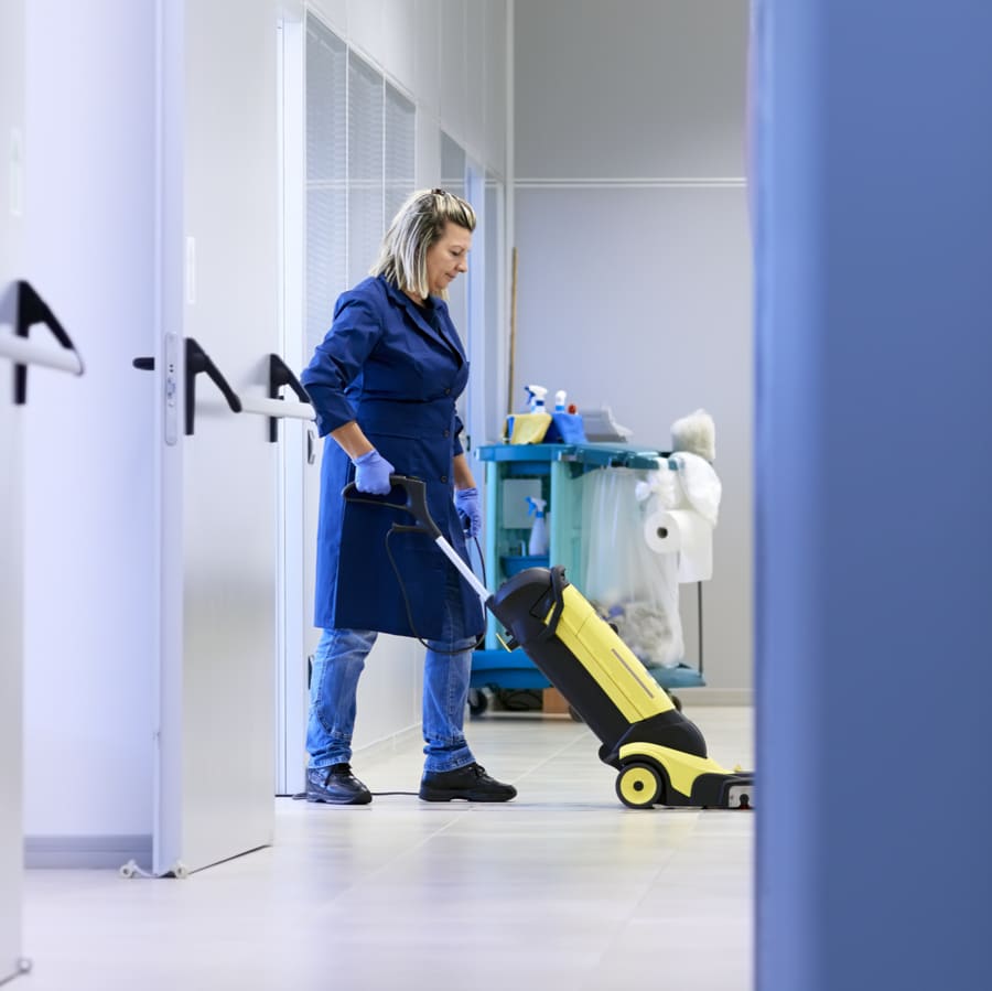 A cleaner running a floor scrubber along a pharmacy corridor