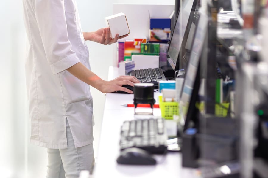 A pharmacy assistant checking a medication box against the order on screen