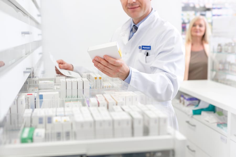A pharmacist reading a medication box at a counter of stocked trays