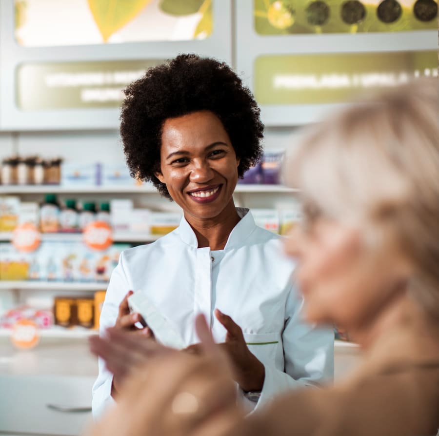A pharmacist serving a customer in front of stocked front-of-store shelves