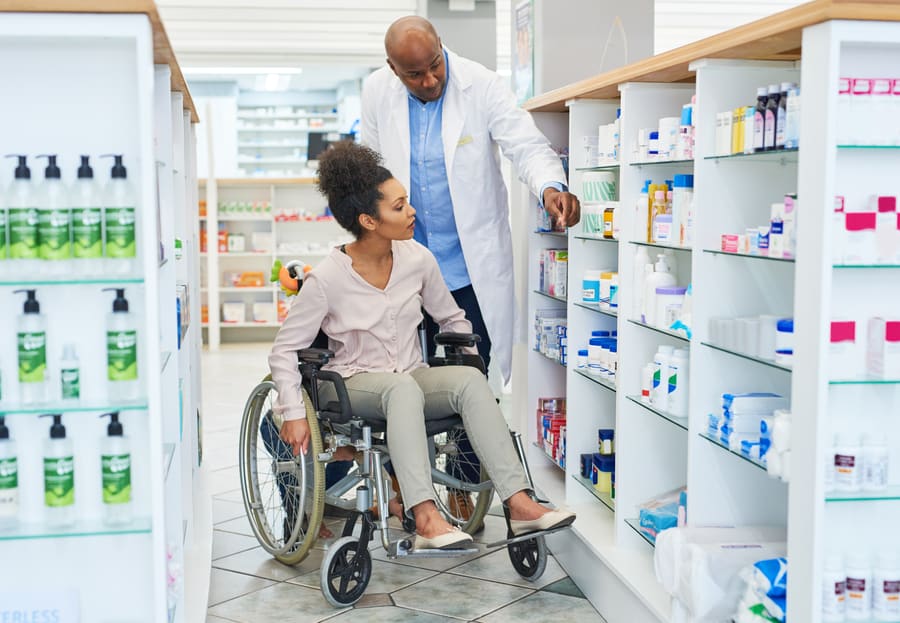 A pharmacist helping a patient in a wheelchair reach a product